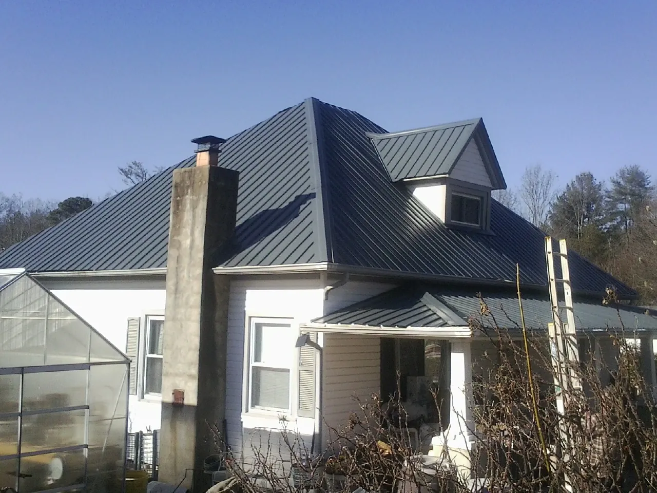 Dark blue standing seam metal roof on a white farmhouse with dormer — Slate & Tile Roof Repair by Roofing Brothers in Chataignier
