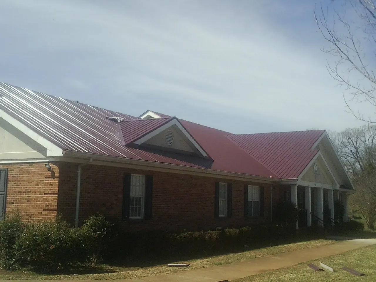 Red metal roof with gabled entries on a long brick building, from a Hail Damage Roof Repair job in Chataignier