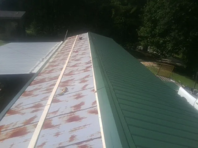 Old rusted panels beside newly installed green metal roofing — Wind Damage Roof Repair by Roofing Brothers in Chataignier