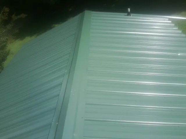 New green metal panels meeting at the ridge of a roof — Flat Roof Repair work by our crew in Chataignier