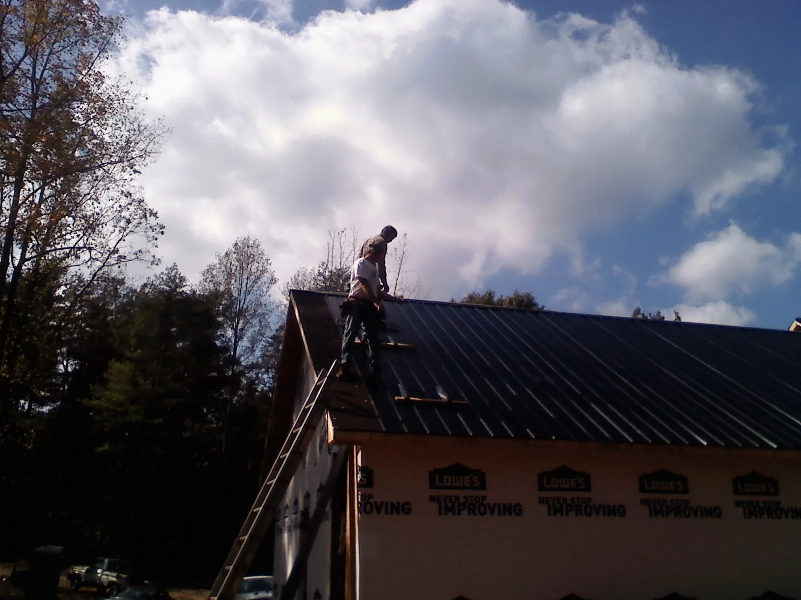 Roofer fastening dark metal panels high against a cloudy sky, from a Roof Inspection job in Chataignier