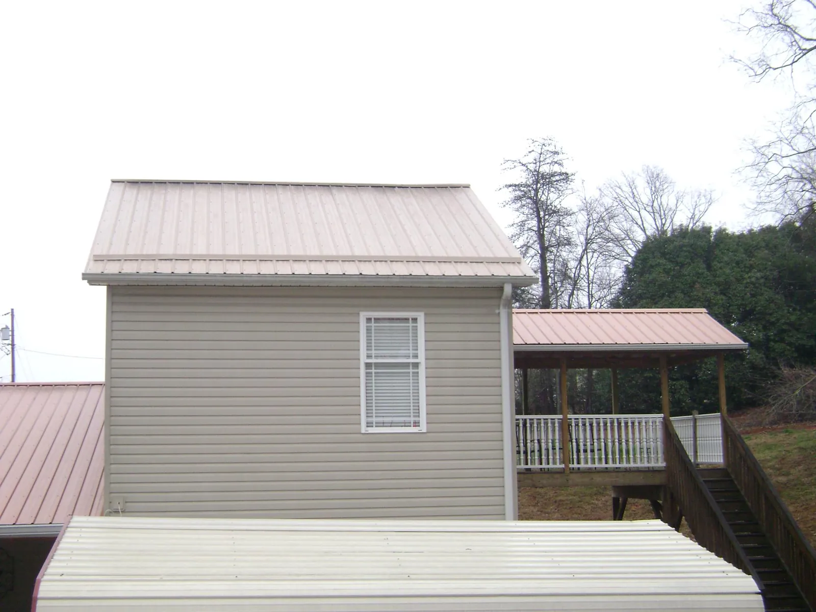Tan metal roofs on a two story addition and attached porch, from a Roof Replacement job in Chataignier